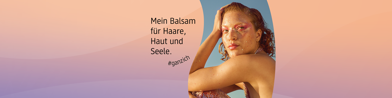 Person mit rötlichem, gewelltem Haar sitzt entspannt vor klarem Himmel mit dem Text ‚Mein Balsam für Haare, Haut und Seele. #ganzich auf pastellfarbenem Hintergrund